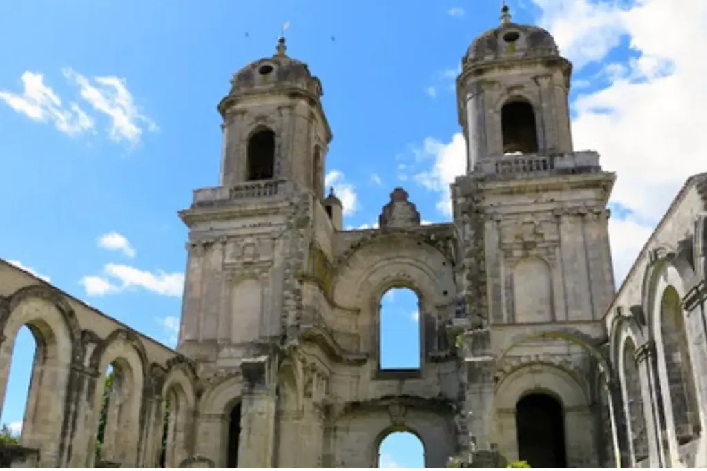 Façade majestueuse de l'Abbaye Royale de Saint-Jean-d'Angély avec ses deux tours symétriques en pierre sculptée s'élevant vers un ciel bleu parsemé de nuages.