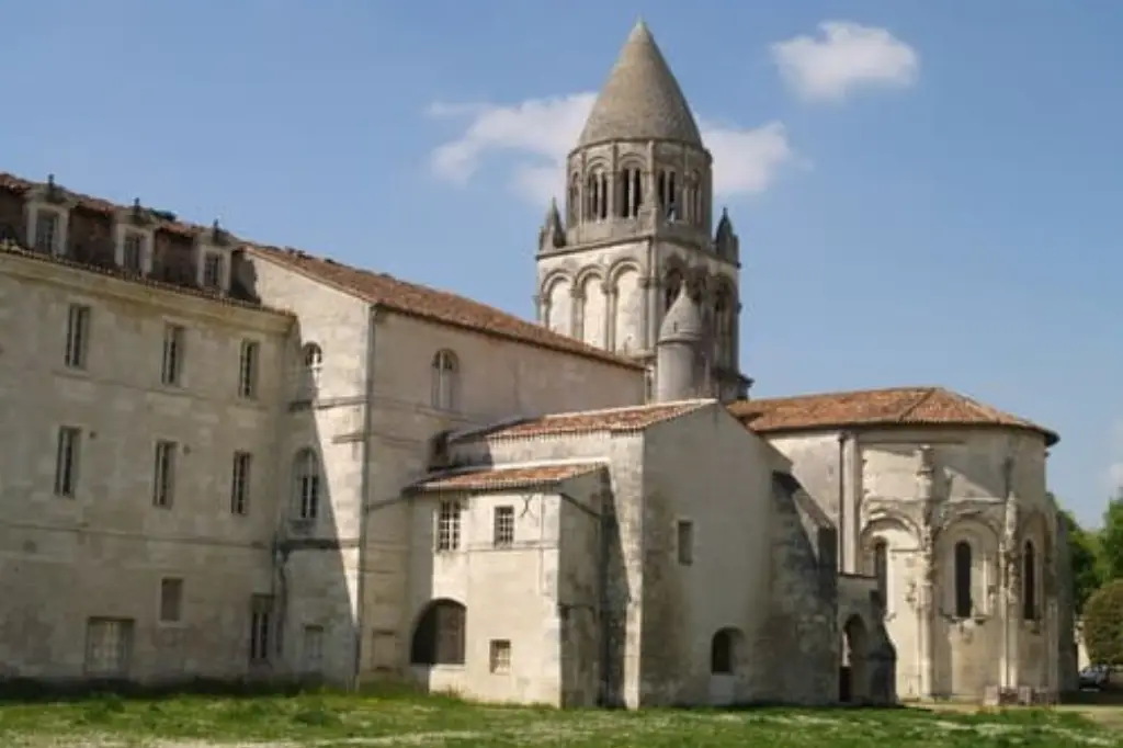 Vue de l'Abbaye aux Dames de Saintes montrant son portail roman richement sculpté et son célèbre clocher à lanternon, sous un ciel bleu dégagé.