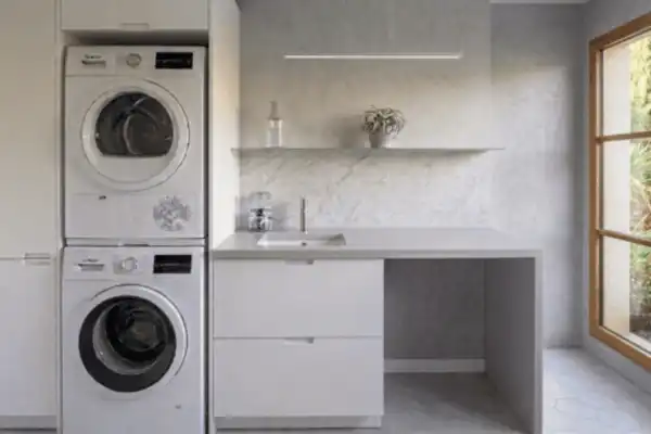 Espace buanderie moderne au Domaine d'Angély avec lave-linge et sèche-linge superposés, plan de travail propre et évier pour le nettoyage du petit matériel.