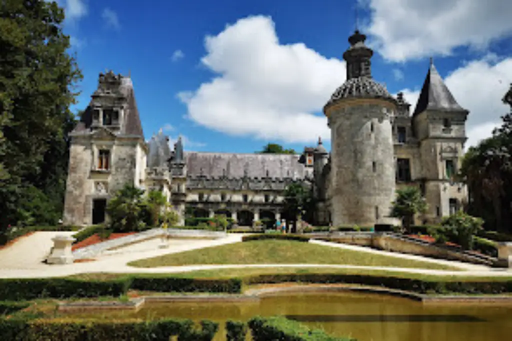 Vue du Château d'Usson (Château des Énigmes) à Pons, une magnifique bâtisse de la Renaissance avec ses tours sculptées, située dans un parc arboré avec des jardins à la française et un bassin au premier plan.