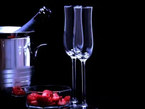 Coffret romantique au Domaine d'Angély comprenant un seau à glace en inox avec une bouteille de champagne, deux flûtes élégantes et une coupelle de fraises fraîches découpées sur fond noir.