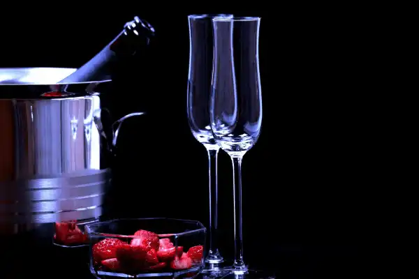 Coffret romantique au Domaine d'Angély comprenant un seau à glace en inox avec une bouteille de champagne, deux flûtes élégantes et une coupelle de fraises fraîches découpées sur fond noir.