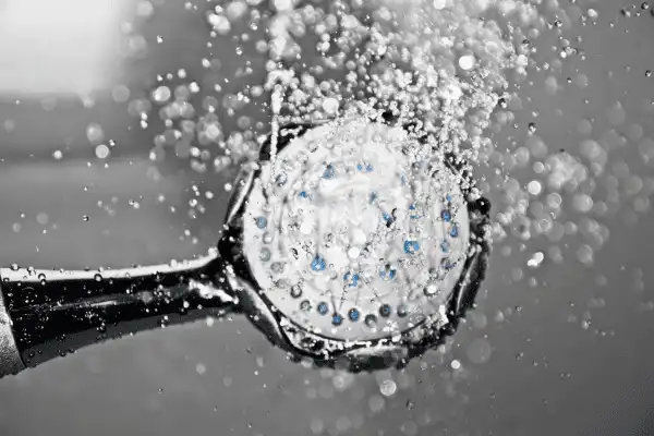 Gros plan sur un pommeau de douche chromée moderne diffusant des filets d'eau claire et scintillante sur un fond sombre et élégant.