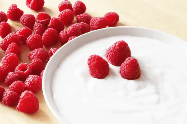 Bol de fromage blanc fermier onctueux surmonté de granola croustillant, de myrtilles, de framboises et d'une feuille de menthe fraîche, servi sur une table en bois.