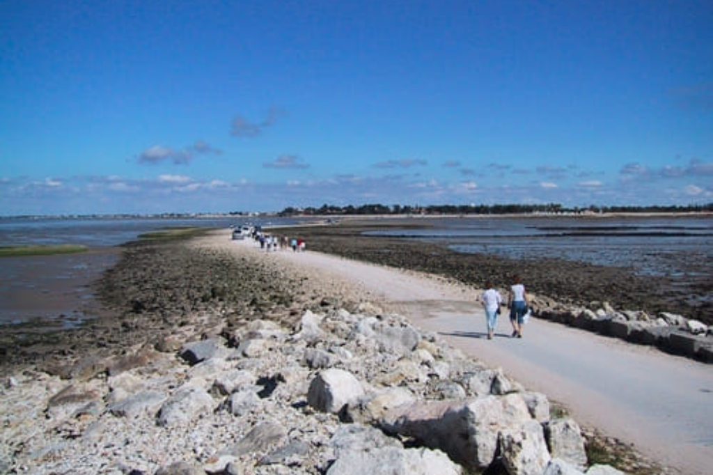 Vue de la Passe aux Bœufs à marée basse, un chemin de sable et de pierres se découvrant entre deux étendues d'eau pour mener à l'Île Madame, sous un ciel de fin de journée.