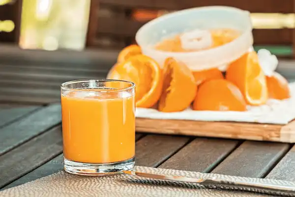 Un verre de jus d'orange frais pressé à la main, posé sur une table en bois avec des oranges de Sicile coupées et un presse-agrumes en arrière-plan.