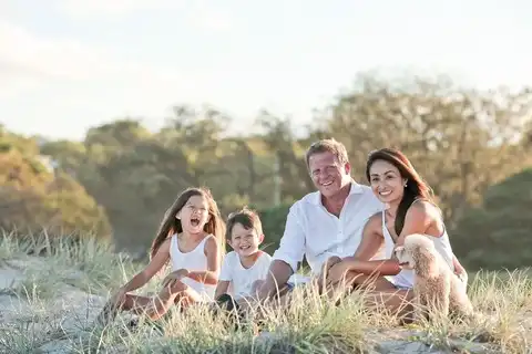 Photo de la famille Leroy, un couple de parents souriants assis dans l'herbe avec leurs deux enfants rieurs.