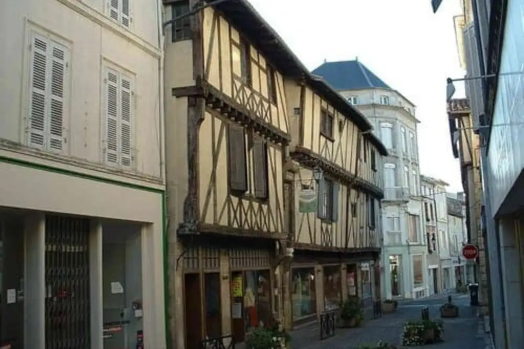 Vue d'une rue pavée dans le centre historique de Saint-Jean-d'Angély, mettant en avant une maison médiévale à colombages avec des pans de bois croisés et des volets bruns.