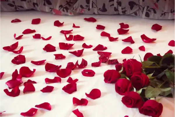 Des pétales de roses rouges étalés sur un sol blanc avec en premier plan un bouquet de roses rouges.