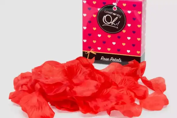 Des pétales de roses rouges artificielles étalés devant la boite qui les a contenus.