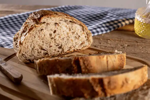 Miche de pain complet artisanal tranchée sur une planche en bois, révélant une mie riche en céréales, préparée par la boulangerie Le Délice des Anges.