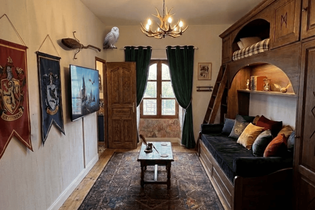Salon et dortoir pour enfants de la suite Harry Potter au Domaine d'Angély. Structure de lit superposé en bois massif, canapé bordeaux, tapis aux motifs magiques, bannières de Gryffondor et Serdaigle, et une chouette blanche décorative.