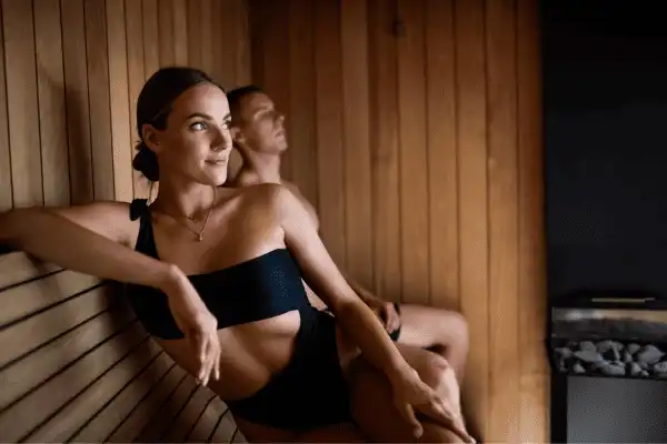 Un homme et une femme se relaxant côte à côte sur les bancs en bois d'un sauna chaleureux, les yeux fermés, profitant de la chaleur purifiante.