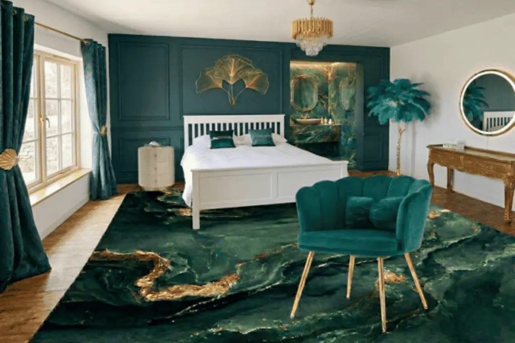 Vue d'ensemble de la suite Art Déco du Domaine d'Angély à Saint-Jean-d'Angély. On y voit un grand lit blanc king-size, un tapis vert émeraude à motifs de marbre doré, un fauteuil en velours coquillage, et un lustre en cristal doré. La chambre comprend une salle de bains ouverte.