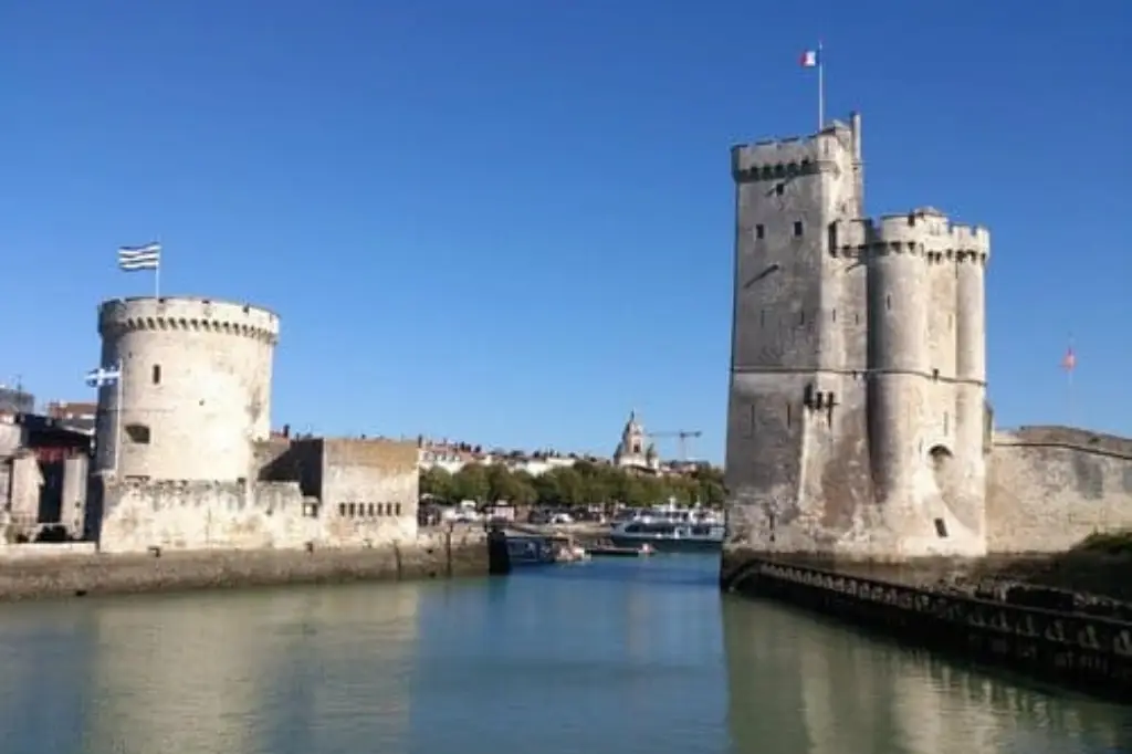 Les deux tours médiévales de La Rochelle, la tour Saint-Nicolas et la tour de la Chaîne, encadrant l'entrée du Vieux-Port sous un ciel bleu intense, avec des drapeaux flottant à leurs sommets.